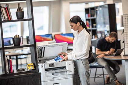 Woman in office scanning document, book shelves, table, chairs, man in background