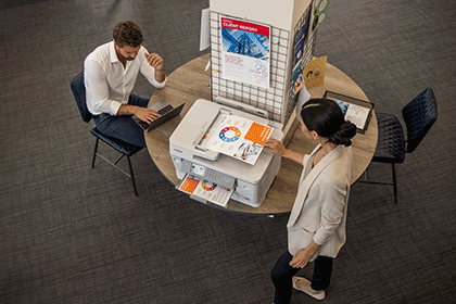 Aerial view of man and woman in office, colour documents on printer, table, chairs