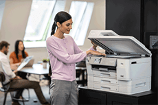 Woman in office copying document, people working in background