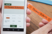 Someone using a smartphone to print an orange label with the words "Thomas Roberts"