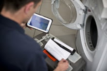 Serviceingeniør ved en vaskemaskin holder i et nettbrett og skriver ut på en mobil skriver i Brother PJ700 serien