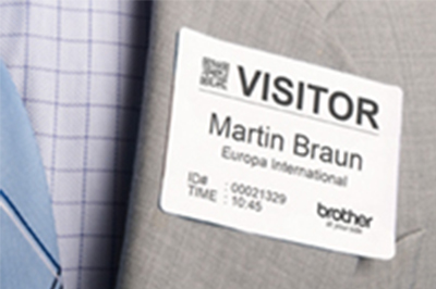 Brother DK-11234 visitor badge label attached directly to grey suit jacket