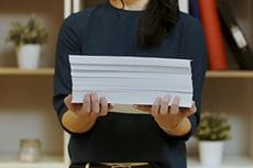 En person holder en bunke papir med begge armene
