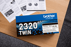 En eske med Brother original TN2320TWIN sort toner Twin Pack ligger på et bord  sammen med dokumenter i sort-hvitt