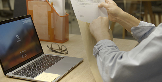 Moški sedi za mizo s prenosnim računalnikom in vstavlja dokumente v kuverto