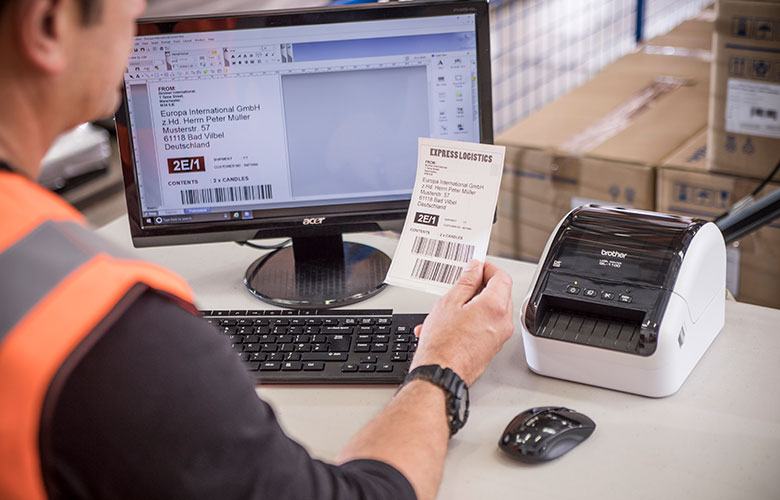 QL-labelprinter på bord ved siden af computerskærm og tastatur
