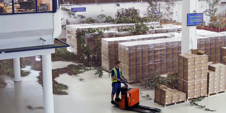 Mann på en mini gaffeltruck i en fabrikk omgitt av bokser og trær
