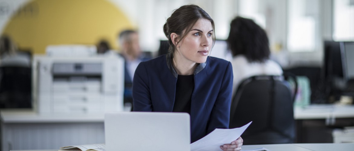 Une femme travaillant sur son ordinateur portable est assise à un bureau avec une imprimante Brother en arrière-plan. 