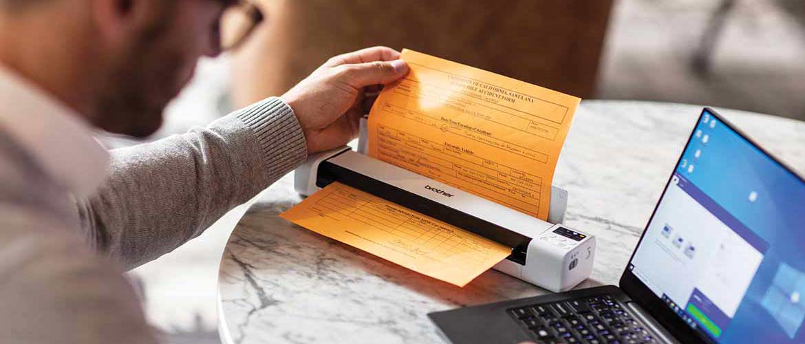 Un homme travaille sur son ordinateur et utilise un scanner portable pour numériser un document