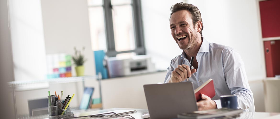 Un homme de bonne humeur travaille à son bureau, équipé d'un ordinateur portable et d'une imprimante wifi.  