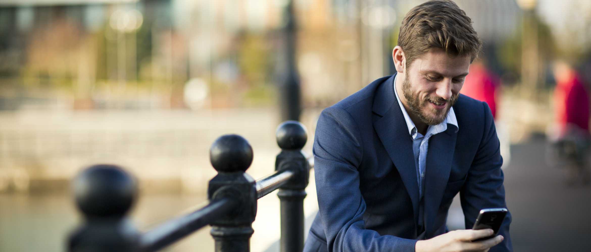 Un jeune homme en costume consulte son téléphone portable dans la rue.