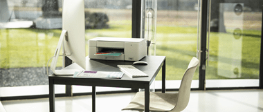 Au premier plan un bureau avec un ordinateur ainsi qu'une imprimante jet d'encre Brother 