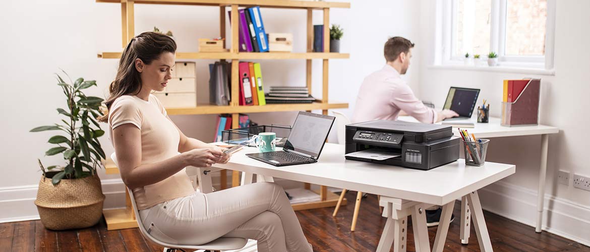 Une femme travaille sur une table équipée d'un ordinateur portable et d'une imprimante