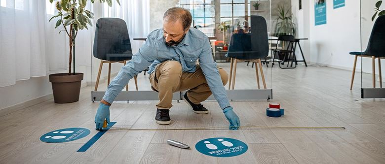 Un homme applique une signalétique au sol pour instaurer les mesures sanitaires et de distanciation sociale en entreprise.