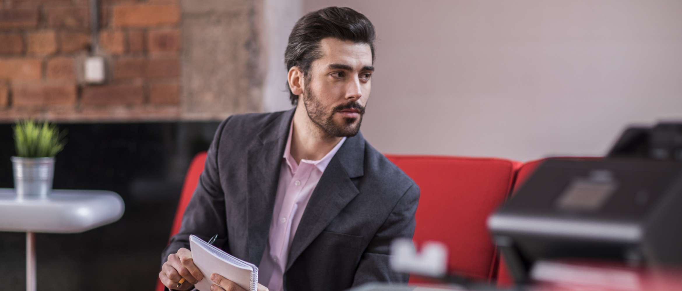 Un homme assis prend des notes à l'aide d'un bloc de papier tandis qu'au premier plan se trouve un scanner Brother ADS conçu pour le travail à domicile. 