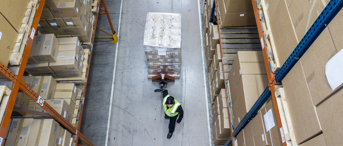 A warehouse employee pulling a trolley of packaged and labelled Brother devices in a warehouse ready for transportation