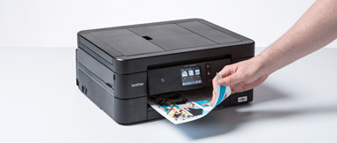 A black Brother MFC printer with a double-sided colour printed output and a hand seen picking the paper up
