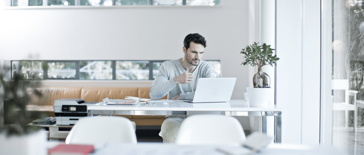 Sur l'image, un homme travaille depuis son ordinateur portable. Il est assis à un bureau.