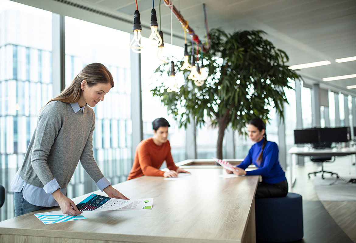 A long desk with a woman looking at documents and two people sat talking