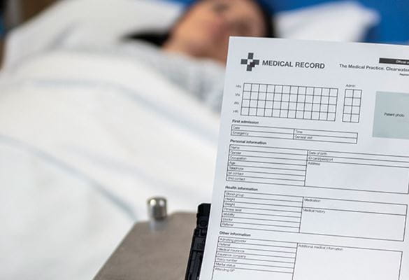 Patiente couchée dans son lit en fond et au premier plan, le scanner ADS-3600W Brother numérisant le dossier médical du patient
