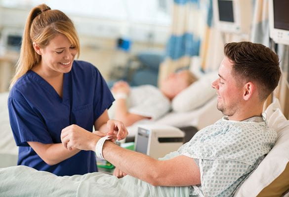 Infirmière en uniforme bleu posant le bracelet sur un patient assis dans son lit