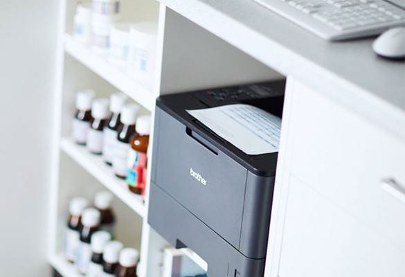 Imprimante laser mono Brother HL-L2375DW dans une pharmacie sous le comptoir à côté des médicaments
