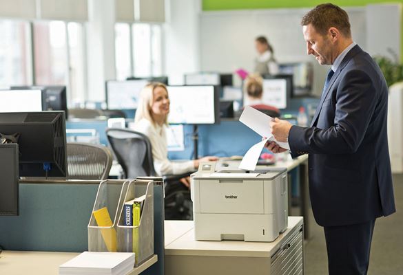 Un homme en costume bleu dans un bureau partagé qui vient chercher ses documents imprimés par une imprimante Brother