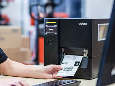 Main récupérant une étiquette imprimée par une imprimante d’étiquettes industrielles Brother