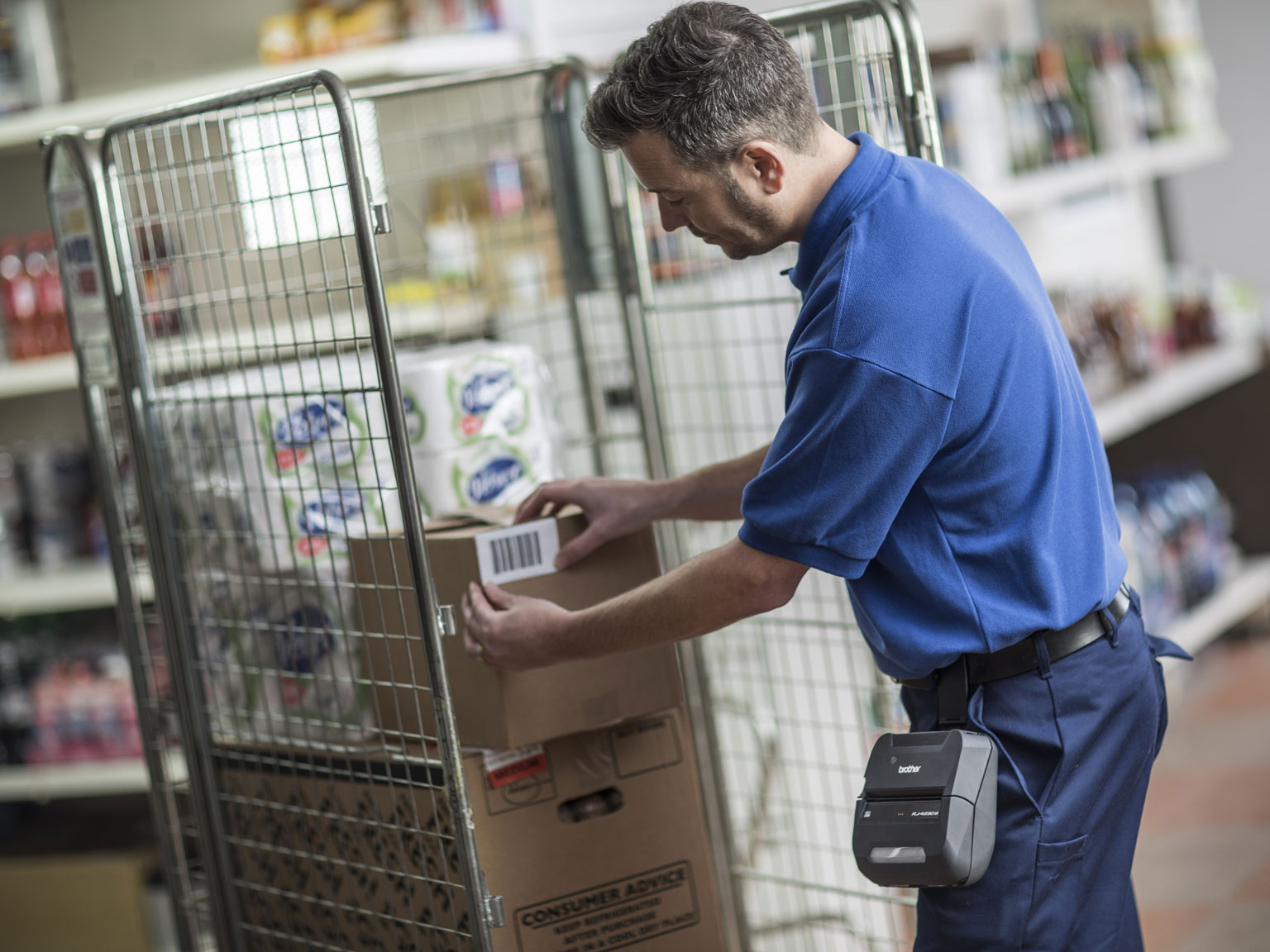 Employé d’entrepôt appliquant une étiquette avec code-barres sur une carton/colis, qui a été imprimée sur l’imprimante portable Brother RJ