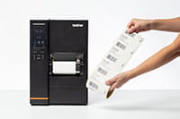 Rouleau d'étiquettes pré-imprimées présenté à côté de l'imprimante d'étiquettes industrielle TJ