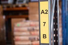 Yellow printed label affixed to metal shelving unit in a warehouse