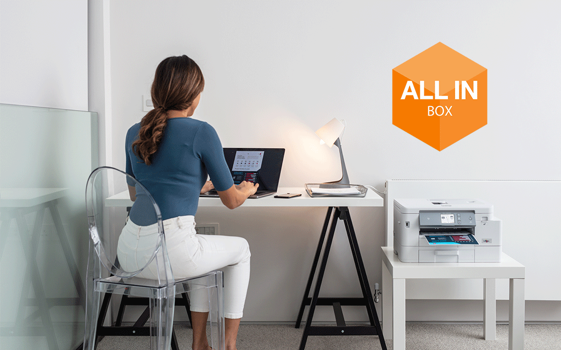 Femme assise à son bureau en télétravail avec le logo All in Box incrusté au dessus de l'imprimante