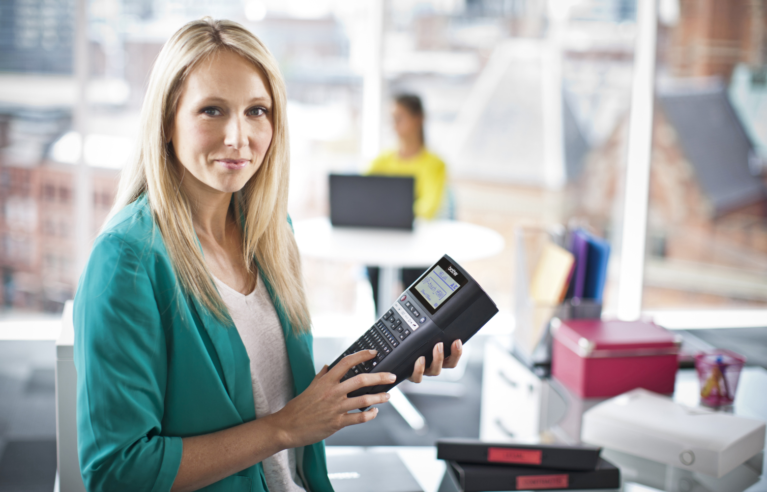 Une femme responsable des installations tenant une imprimante d'étiquettes Brother P-touch en préparation de l'étiquetage des articles dans le bureau