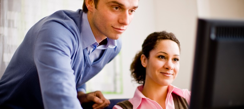 Coworker leaning over a females shoulder to use the computer