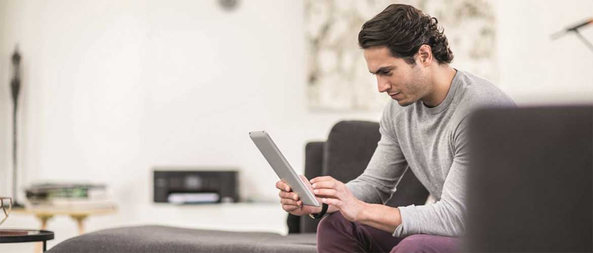 Uomo con tablet sul divano di casa. Stampante Brother sul mobile