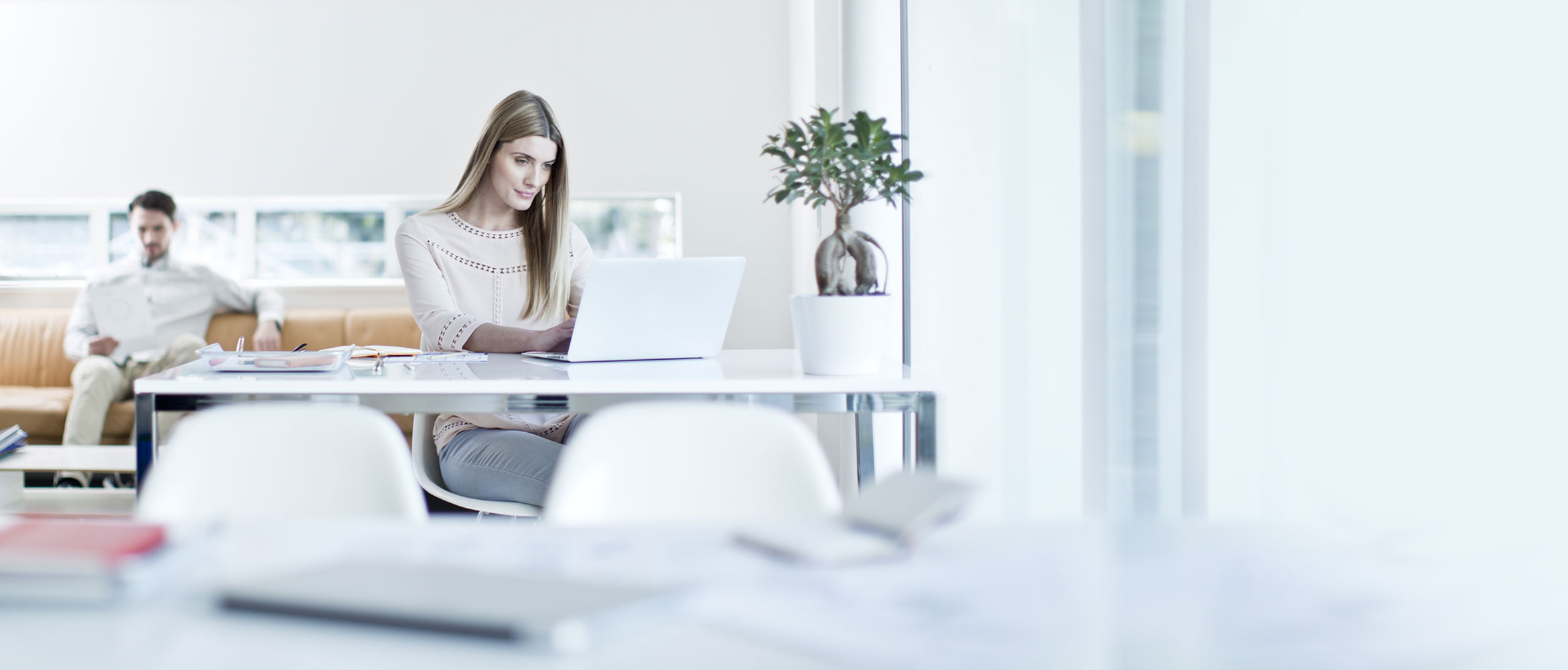 Ragazza al lavoro al PC mentre un ragazzo è seduto sul divano