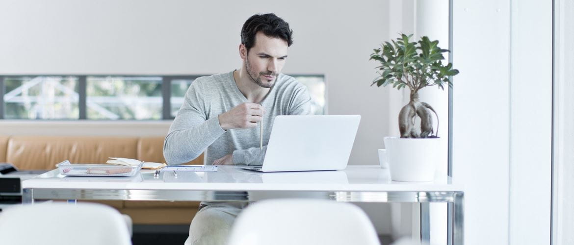 Ragazzo con maglietta grigia al lavoro al suo PC portatile in un ufficio moderno