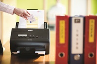 Scanner Brother ADS-2400N in azione con a fianco raccoglitori di documenti