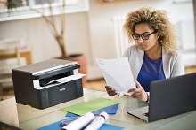 Ragazza al lavoro nel suo ufficio in casa con foglio stampato da stampante multifunzione laser Brother DCP1612W