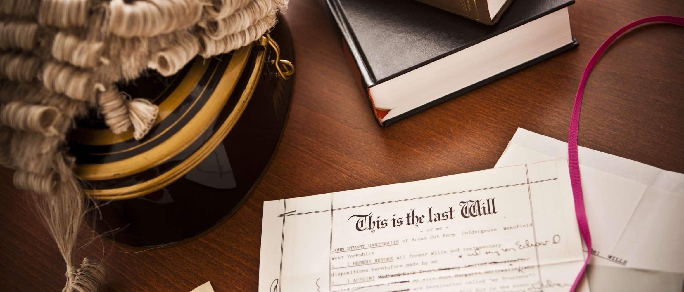 A legal document is on a table in a law office next to a lawyer's courtroom wig and various books 