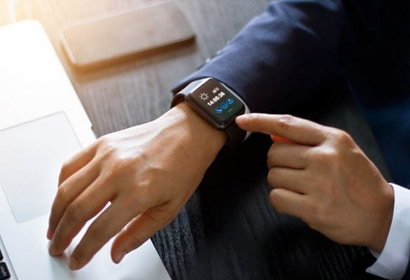 A man in a suit jacket is seen using wearable technology in the form of a smartwatch in the workplace of the future