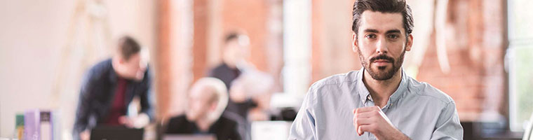 Man wearing shirt in office, people in background talking