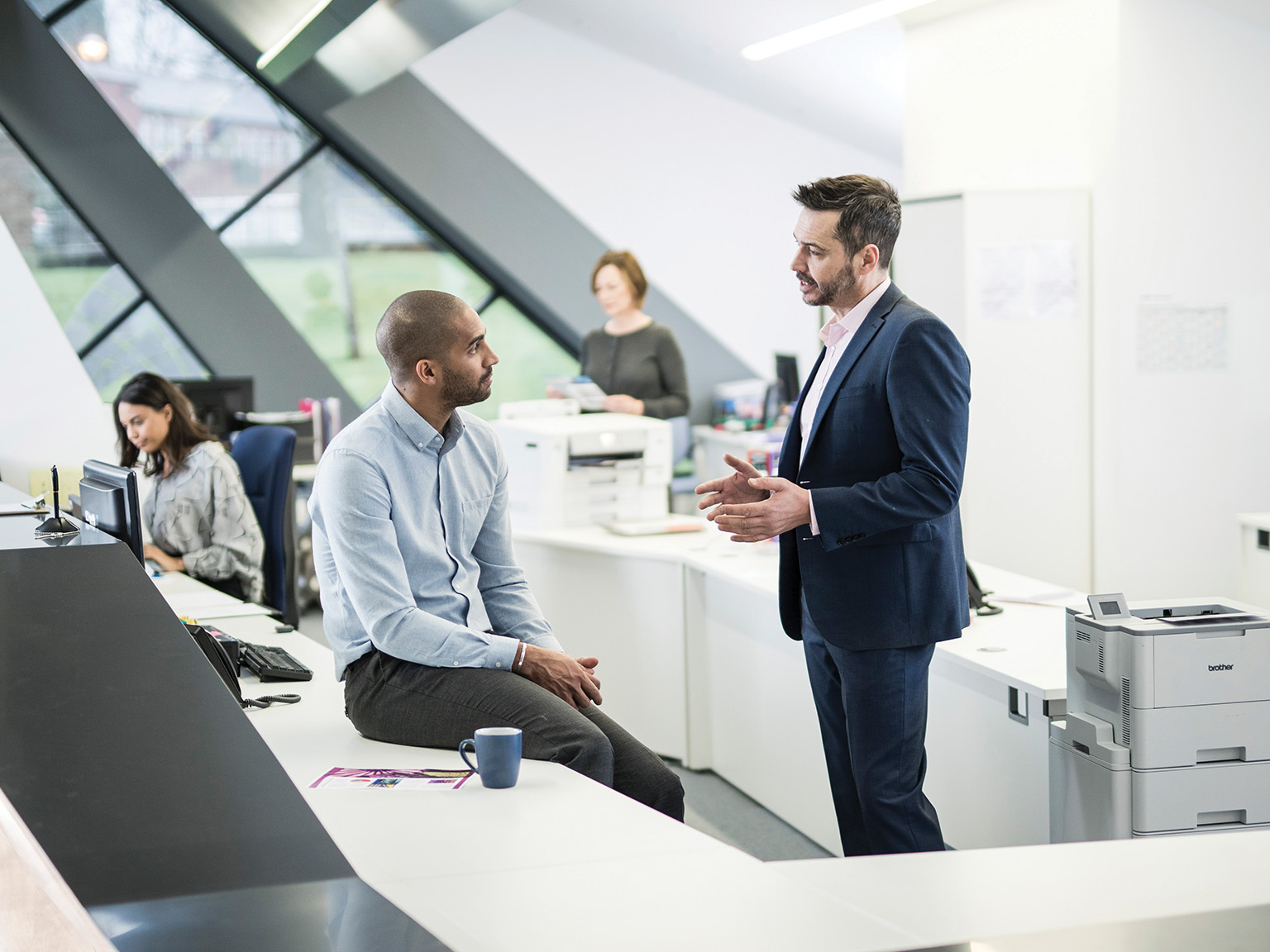 Two guys talking at a desk within an office enviroment