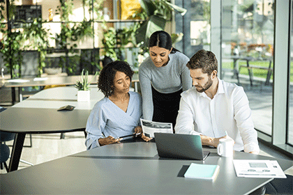Two women and a man sat around table in office, laptop, plants