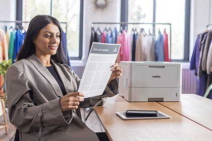Female holding A4 mono document sat at wodden desk, Brother HL-L5210DN, colourful clothes on rails
