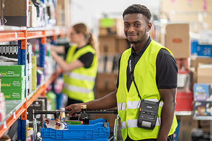 Back of house worker in high vis vest wearing Brother RJ-3200 printer on shoulder strap and smiling to camera