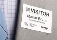 Brother DK-11234 visitor badge label attached directly to grey suit jacket