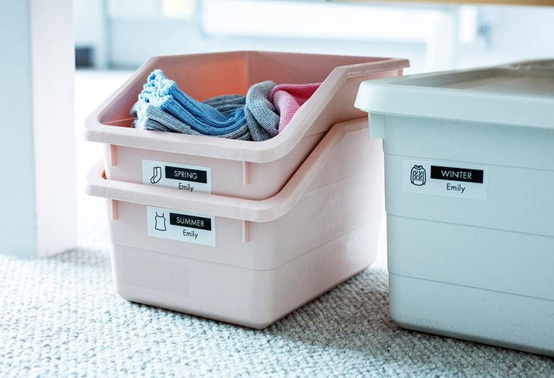 Two pink and one blue box filled with clothes placed under a bed