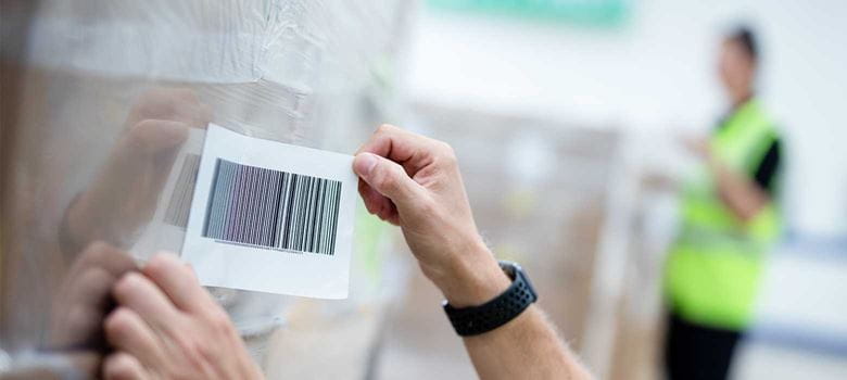 Label with barcode being stuck on boxes with shrink wrap in warehouse