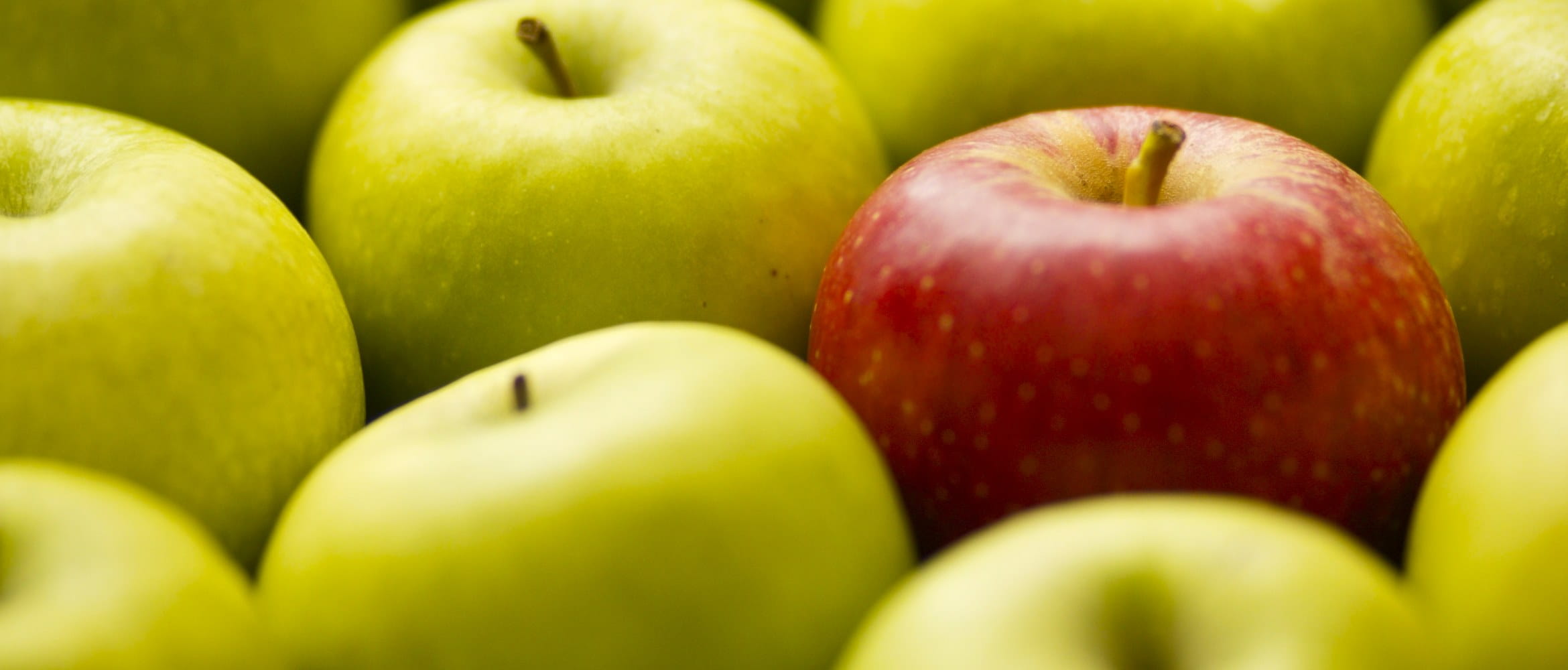 Ett rødt eple skiller seg ut mot et utvalg av grønne epler i en fruktkurv i en dagligvarebutikk